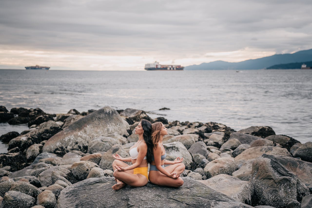 Two women meditating on a rocky coast by the ocean, embracing calmness and mindfulness.